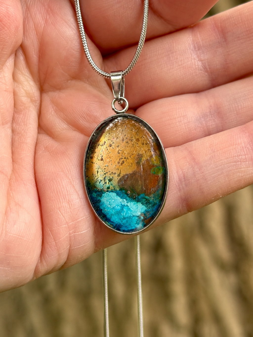 Torchbearer Twelve Specimen One wearable copper specimen pendant featuring vivid verdigris blue formations beneath a weathered copper-gold landscape, preserved between glass and stainless steel.